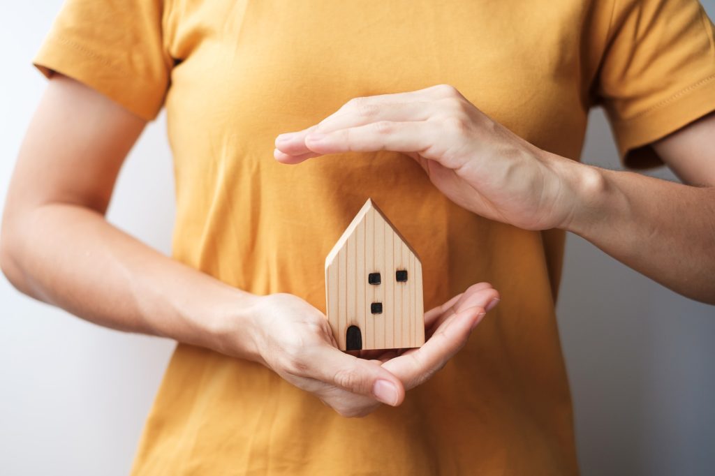 woman hand cover wooden Home model. real estate, insurance and property concepts
